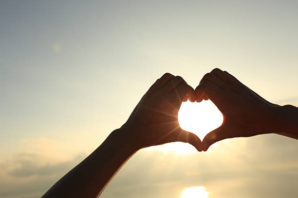 istock Heart shape making of hands against bright sea sunrise 498659652