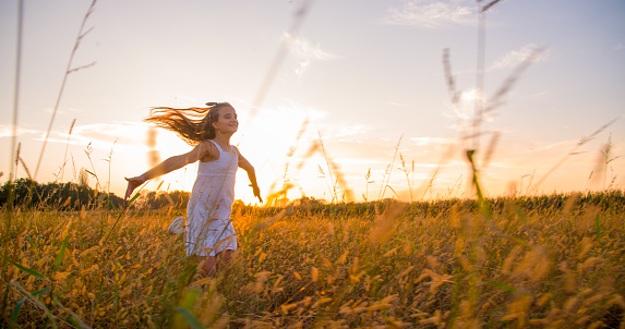 Little girl running with outstretched arms in a meadow at sunset.