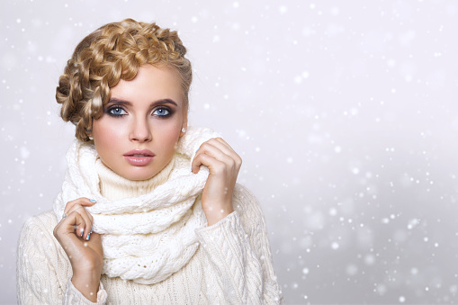 portrait of a beautiful young blonde woman on a light background. hair tied in a braid. girl wearing a warm sweater and scarf. copy space.