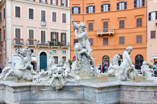 Rome, Italy - April 19, 2015: The Fountain of Neptune, Fontana del Nettuno, stands at the north end of Piazza Navona, Rome, Italy. The Piazza was regularly flooded between 1652 and 1866 on the weekends in August for games, including Roman Naval games.  Today it is a constantly moving town square, with street performers, Christmas markets and sidewalk cafes.  The Fountain of Neptune has a base made of white marble that was designed by Giacomo della Porta, but 300 years later Antonio Della Bitta added the sculpture of Neptune fighting an octopus to balance out the piazza, because the Moor Fountain at the south end had sculptures, as did Bernini's masterpiece in the center of Piazza Navona...the Fountain of the Four Rivers.