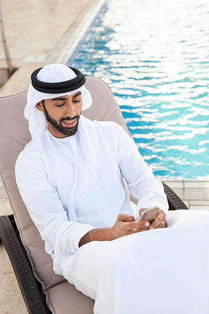 istock Arab Man Browsing Social Media by the Poolside Using Phone 498691868