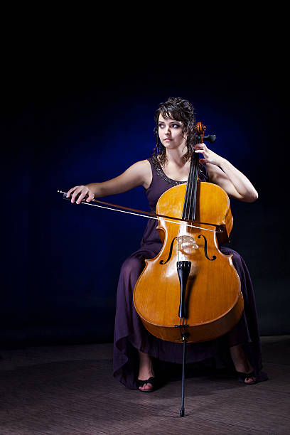 Beautiful girl plays the cello in a concert dress on a dark background.