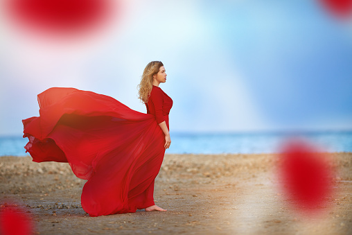 side view of attractive woman on the beach with flying red dress.wilderness, freedom and fashion.