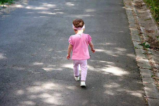 Little baby girl walking away on the road.