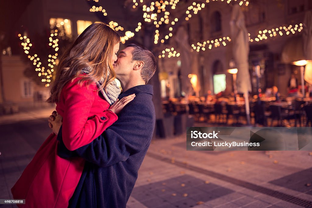 Young affectionate couple kissing tenderly Young affectionate couple kissing tenderly on Christmas street Valentine's Day - Holiday Stock Photo