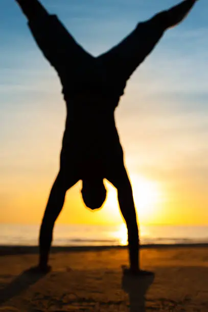 Photo of Defocused silhouette of man making handstand on the beach.