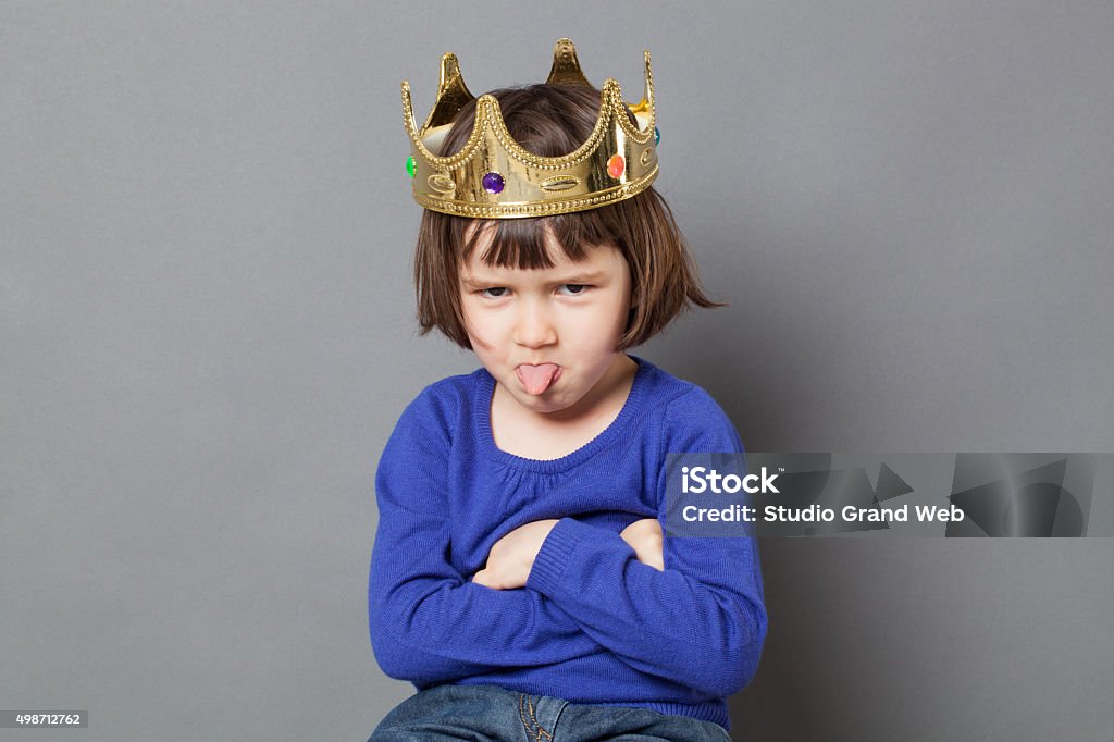 playful preschooler with cheeky attitude and mollycoddled kid crown spoiled kid concept - cheeky preschool child with golden crown on head folding arms and sticking out tongue for disrespectful mollycoddled little king or queen metaphor,studio shot Child Stock Photo