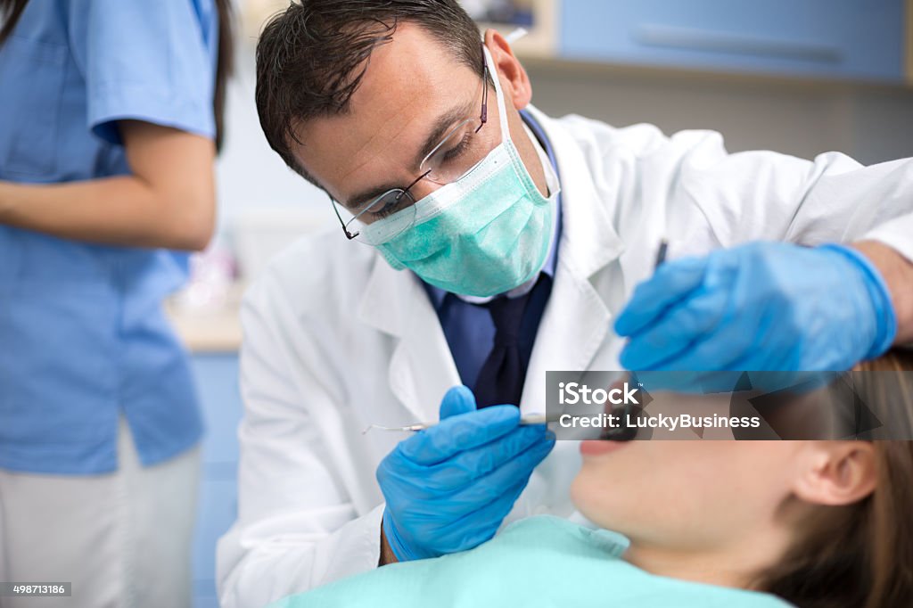 Dentist with protective mask and gloves repair tooth Dentist with protective mask and gloves repair tooth of his young female client at ambulant 2015 Stock Photo