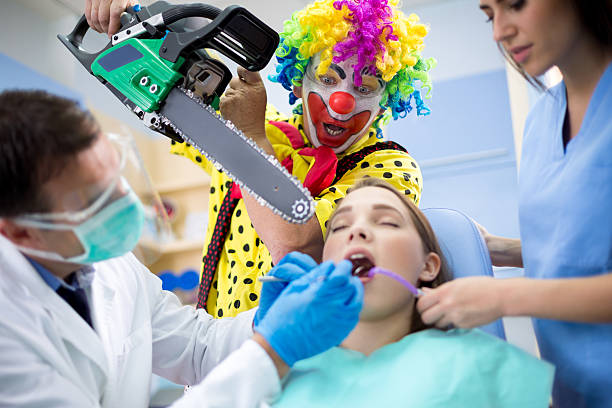 Clown threaten girl with chainsaw in dental ambulant Crazy clown threaten girl in dental chair with chainsaw in dental ambulant ambulant patient stock pictures, royalty-free photos & images