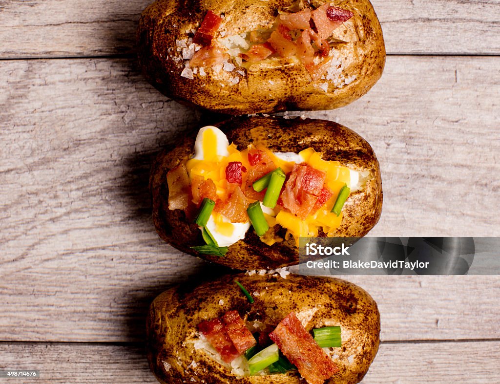 Power Trio! Three baked potatoes, on wooden slats, dressed with bacon, cheddar cheese, sea salt, sour cream and chives. Baked Potato Stock Photo