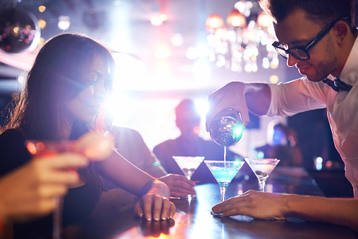 Barman pouring alcohol pouring cocktail for attractive girl