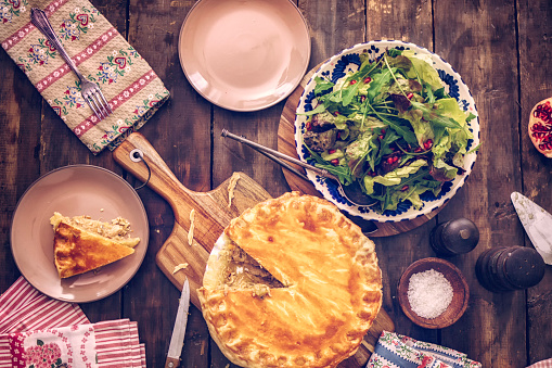 Delicious homemade chicken meat pie with carrots, onion, mushrooms and celery. The pie is served on a plate with green salad.