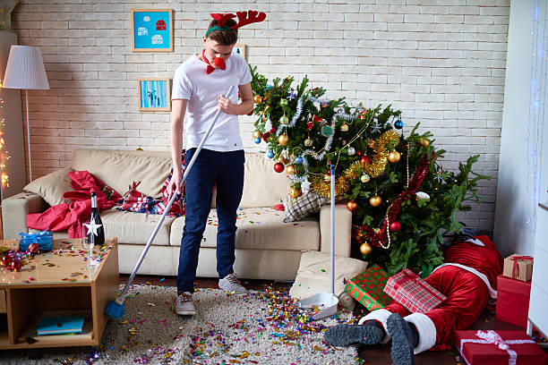 Funny cleaner Young man tidying up living room after party christmas chaos stock pictures, royalty-free photos & images