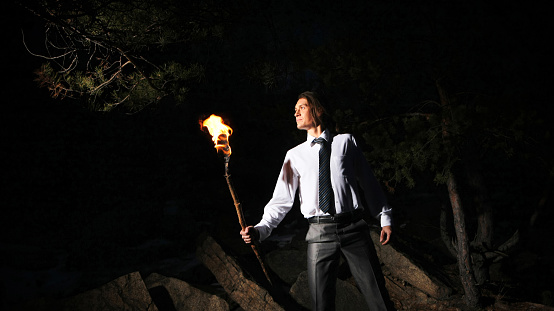Image of brave man holding burning stick while moving in darkness