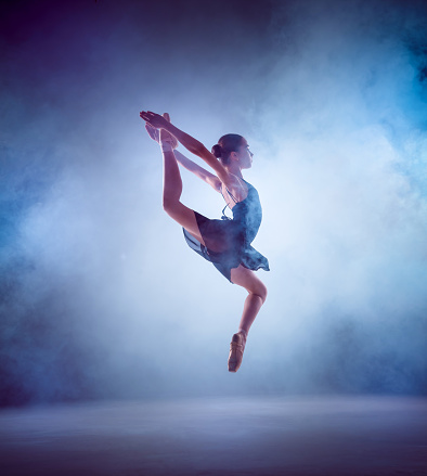 The silhouette of young ballerina jumping on a blue  smoke background.