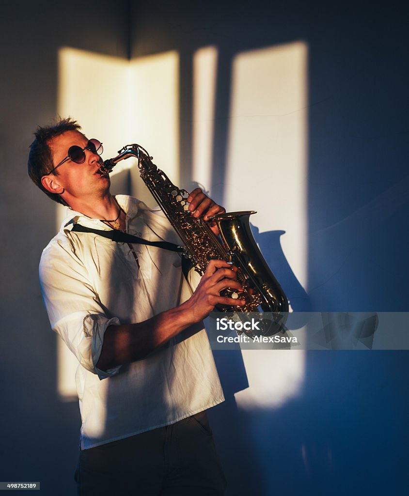 One passionate young saxophone player indoor saxophonist playing his saxophone in the window light in indoor setting  Adult Stock Photo