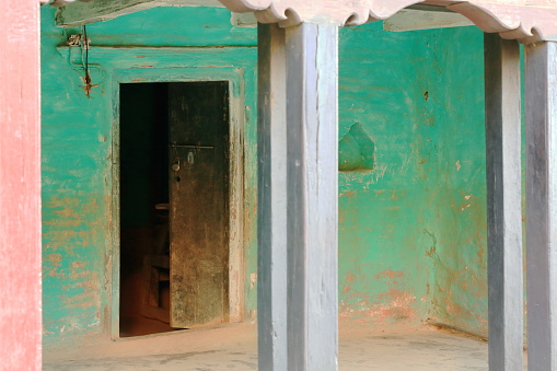 Green painted hallway behind blue painted wooden gate and with faded dark wood door inside. Traditional newari style house in Bandipur-Tanahu district-Gandaki zone-Nepal.