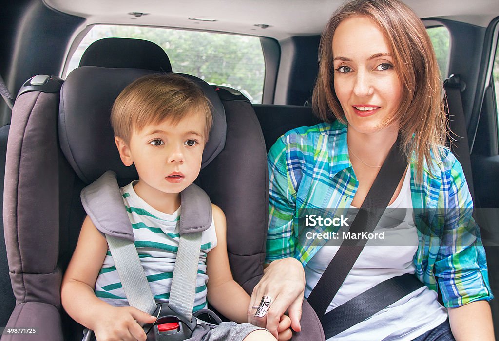 The son and mother are buckled with safety belt. Protection in the car. Caucasian cute son and mother are buckled with safety belt in a car.  Little boy is sitting in the car seat. Woman takes care about kid. Sunny summer day. Vehicle and transportation concept. Activity Stock Photo