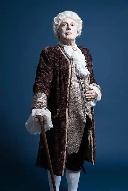 Photo of Retro baroque man with white wig standing with walking stick.
