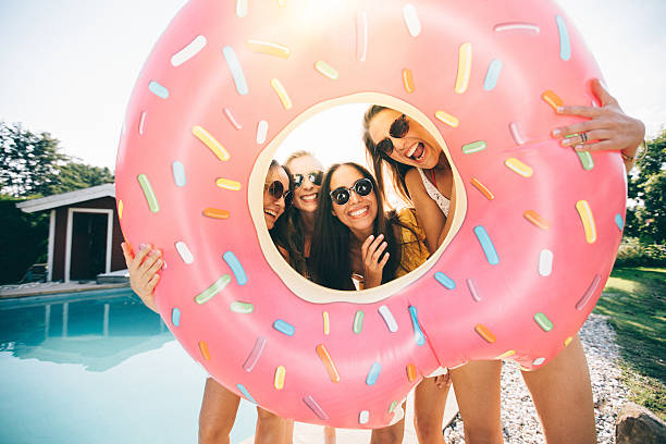 Girls laughing while holding a pool inflatable like a frame Four girls holding a pink pool inflatable around their faces like a frame while laughing together and standing outdoors next to a pool inflatable ring photos stock pictures, royalty-free photos & images