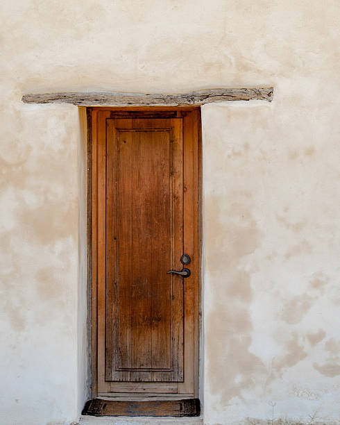 An interesting vertical perspective of an old mission wooden door against a white washed plaster wall     