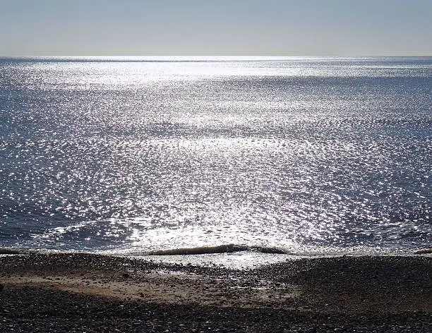Photo showing backlit seaside with sun shining on sea, sparkling water.