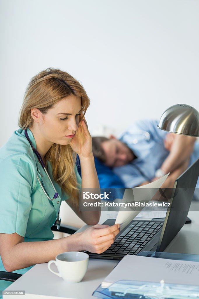 Tired doctor doing paperwork Tired female doctor doing paperwork in hospital 2015 Stock Photo