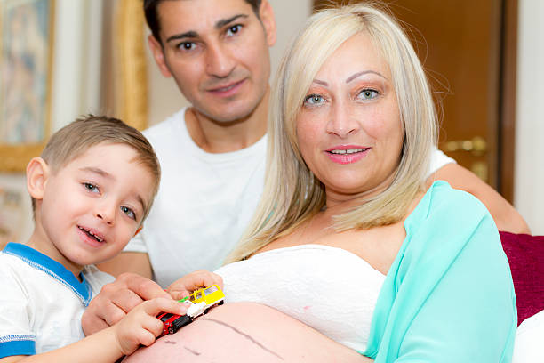 Dad and son playing with toy-cars on mom's belly