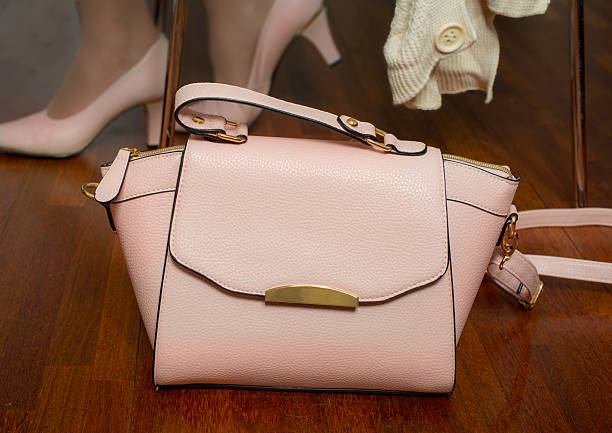 Pink leather purse  next to chair on wooden floor with woman feet  out of focus
