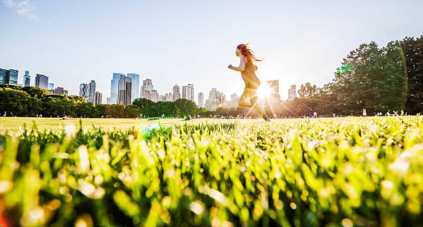 ragazza corre davanti alla skyline di manhattan a central park - prato rasato immagine foto e immagini stock