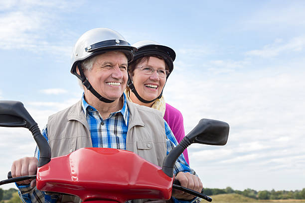 feliz pareja senior de montar un ciclomotor - senior adult action couple motor scooter fotografías e imágenes de stock