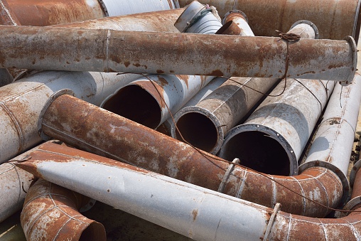 A stack of rusty and damaged industrial pipes and other metal products.