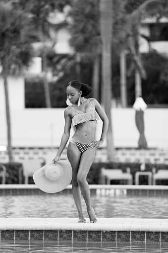 Stock image of a woman in bikini and a hat posing by the pool
