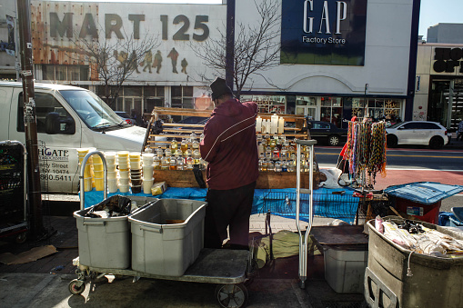 New York City, NY, USA - November 25, 2015: Street vendor on 125th street, Harlem gets his stock ready for sale. Harlem Mart 125 and Gap across the street. 