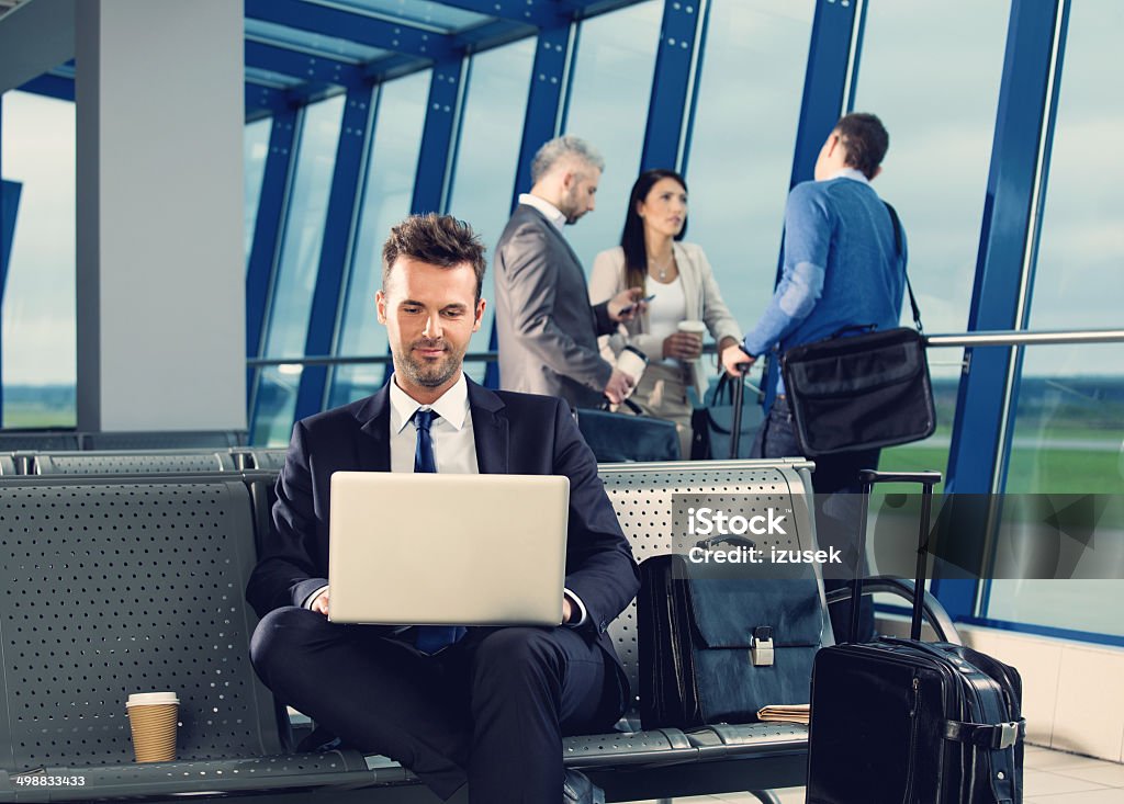 Businessman at the airport People waiting for the flight in the airport lounge. Focus on the businessman using laptop. Airport Stock Photo