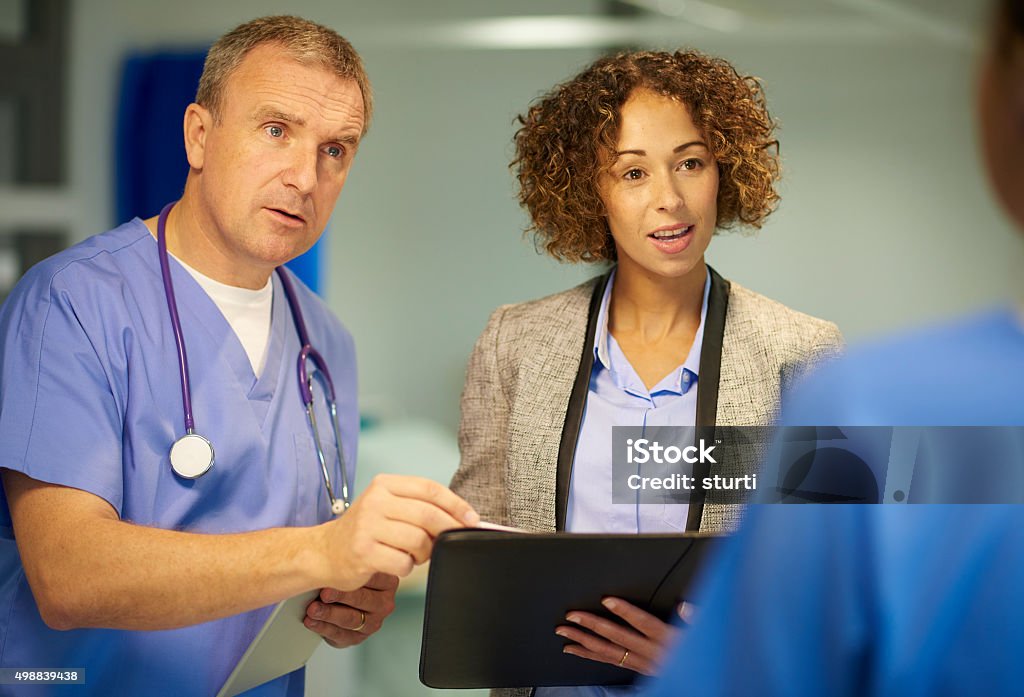 medical  business relationship a mature hospital doctor is chatting with a team of fellow medical professionals , including a suited woman who could be a sales professional or administrator Doctor Stock Photo