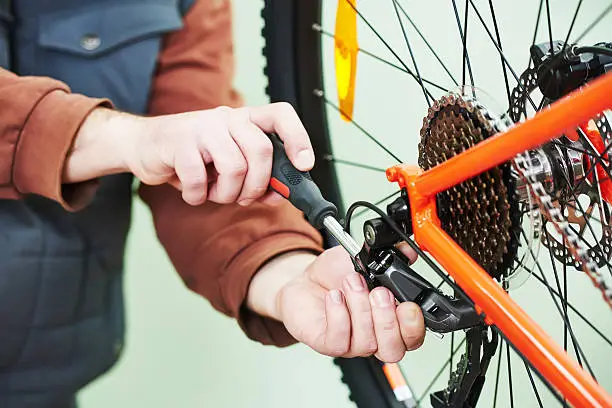 Bike service: mechanic serviceman repairman installing assembling or adjusting bicycle gear on wheel in workshop