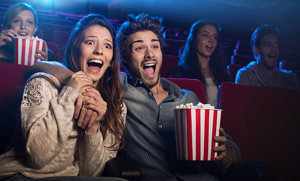 Young couple at the cinema watching an horror movie Young scared couple at the cinema watching an horror movie and screaming, she is holding her boyfriend's hand women screaming surprise fear stock pictures, royalty-free photos & images