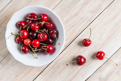 White bowl of fresh cherries on a wooden table