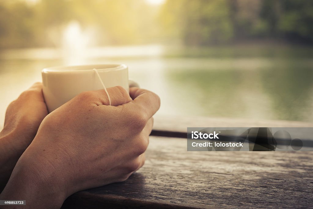 Tea by the lake Closeup on a woman's hands holding a cup of tea by a lake in the afternoon Coffee Cup Stock Photo