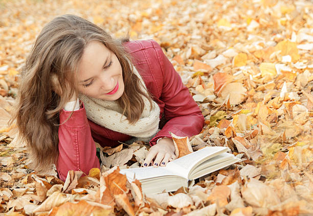 istock Young woman reading in park, sitting on leaves 498859706