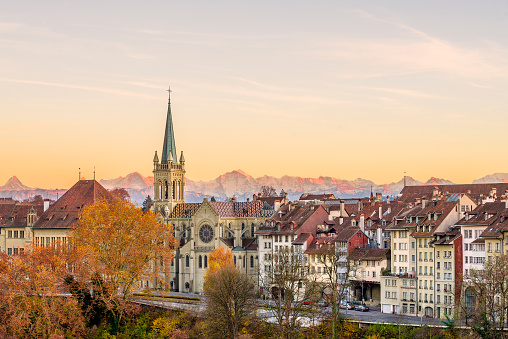 Facades of the old town of Bern, capital of Switzerland, with Swiss alps peaks in the background glowing reddish during an  autumn sunset.