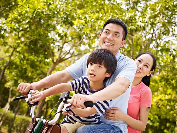 familia asiática montar en bicicleta en el parque - park child asia lifestyles fotografías e imágenes de stock