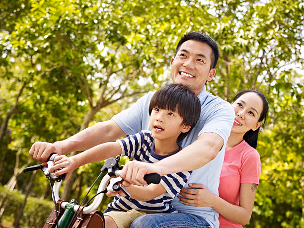 famiglia asiatica bicicletta di equitazione nel parco - park child asia lifestyles foto e immagini stock