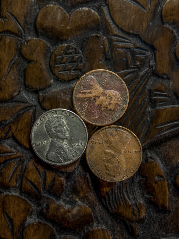 Three old American pennies side by side from the years 1943, 1940, 1936 sitting on top of wood carved flowers.