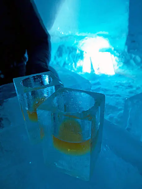 Two Frozen Shot glasses with whiskey made of ice, shaped form frozen water in dark blue ice bar environment