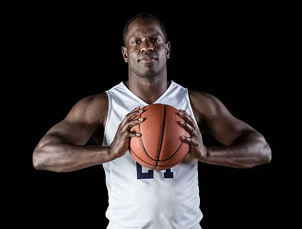 Strong, athletic African American basketball player holding the ball ready to score. Shot on a black background