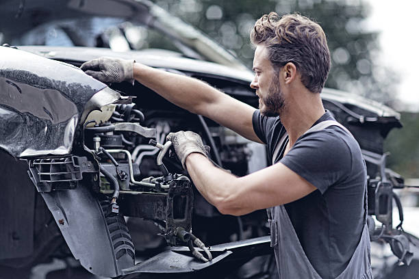 männliche mechaniker arbeiten am auto destroyed - autoschrottplatz stock-fotos und bilder