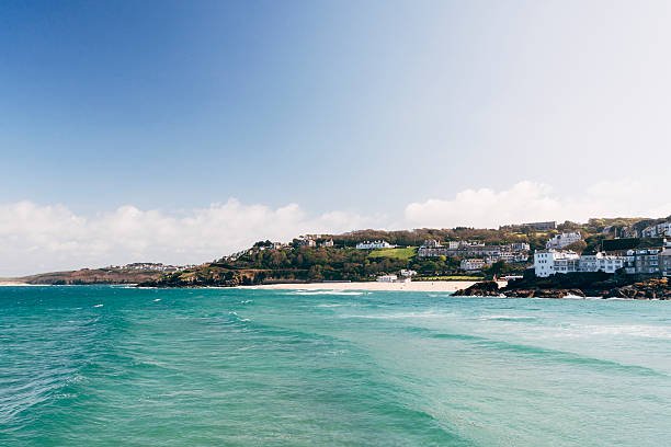 St Ives coastline from the harbour wall in Cornwall St Ives coastline from the harbour wall in Cornwall, England. Porthminster beach is towards the right edge of the frame and Carbis Bay toward the left edge of the frame. In the foreground waves are rolling across the blue sea. st ives cornwall stock pictures, royalty-free photos & images