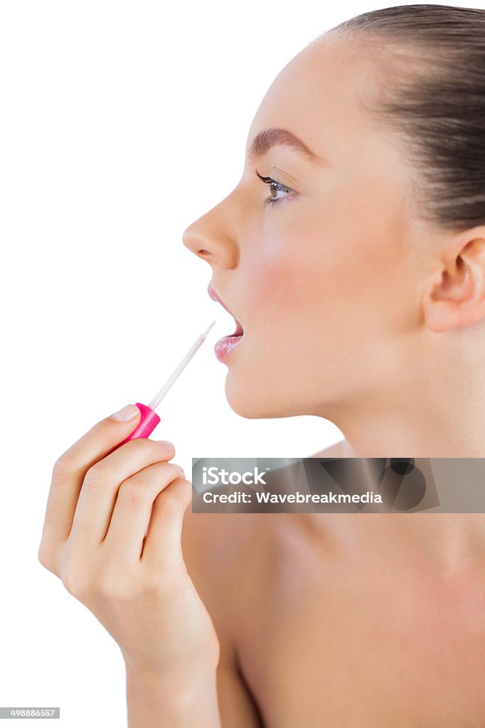 Profile of woman putting lip gloss on her lips Profile of young woman putting lip gloss on her lips against white background Adult Stock Photo